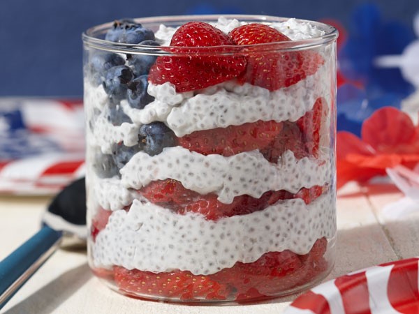 Glass bowl layered with strawberries, yogurt and chia seeds, and blueberries