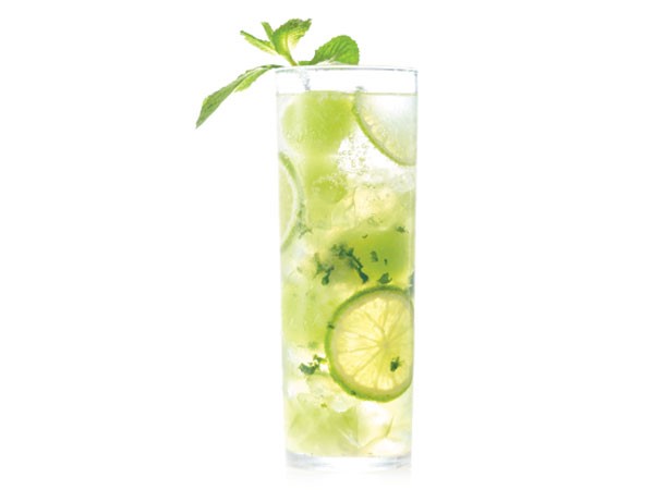 Tall glass filled with honeydew mojito, ice, chunks of honeydew, lime and fresh mint