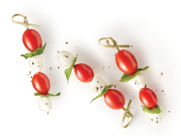 Cherry tomatoes, basil leaves and mozzarella balls on a wooden skewer and covered in freshly ground black pepper