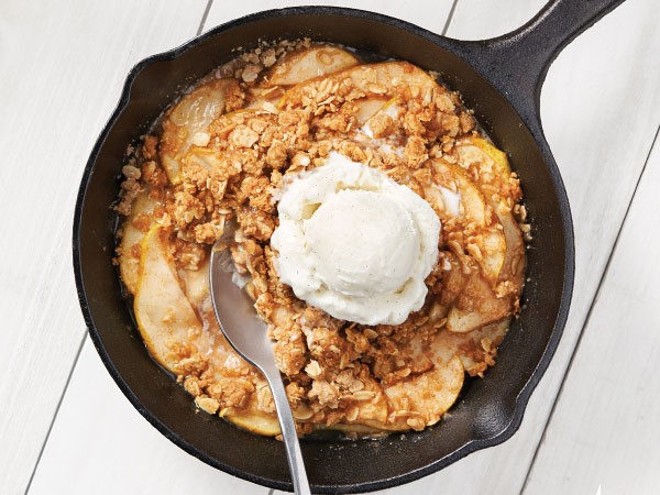 Cinnamon spiced pear crisp served in a cast-iron skillet topped with a scoop of vanilla bean ice cream