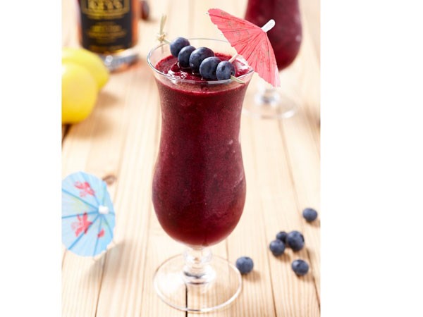 Glass filled with a blueberry-lemon daiquiri, garnished with a pink umbrella and fresh blueberries