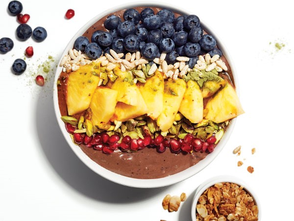 Smoothie bowl topped with pomegranate seeds, nuts, pineapple and blueberries