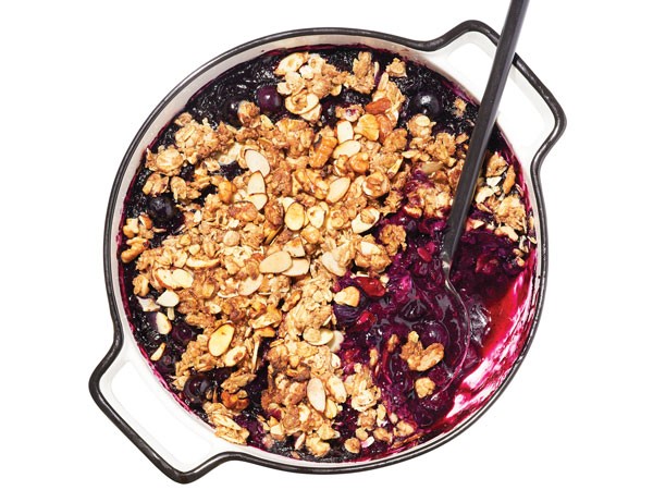 Blueberry-filled dish topped with granola crumble with a serving spoon