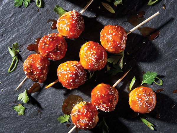 Turkey meatballs covered in sauce and sesame seeds on wooden skewers