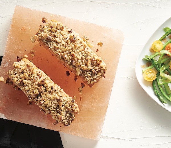 Walnut crusted salmon on a square block next to a plate of veggies on a white background. 