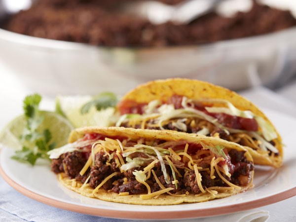 Crunchy shell beef tacos on a plate topped with cheese