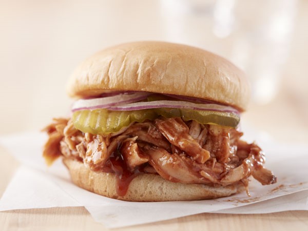 Barbecue chicken on sandwich topped with pickles and red onions