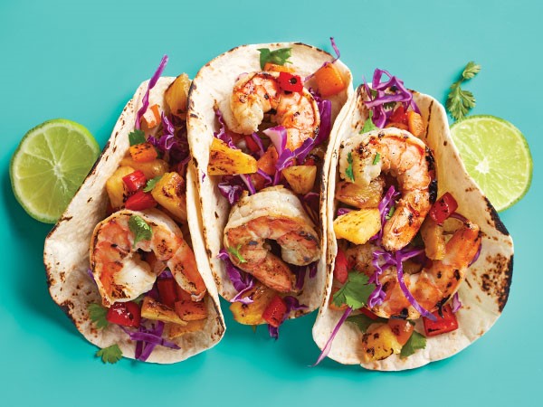 three grilled shrimp tacos in soft shell tortillas with lime slices on the side.