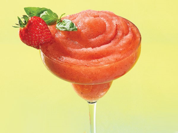 Frozen strawberry margarita in glass with strawberry basil garnish
