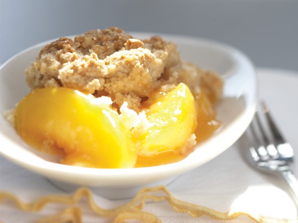 Peach cobbler with oatmeal topping on a white bowl.