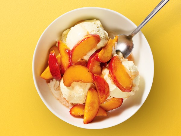 Peach filling over a bowl of vanilla ice cream with a spoon on a yellow background.