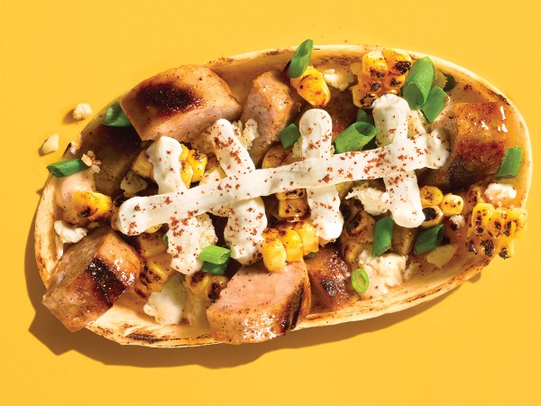 Sliced brats and corn topped with cheese layered to look like football laces in a tortilla bowl on a yellow background.