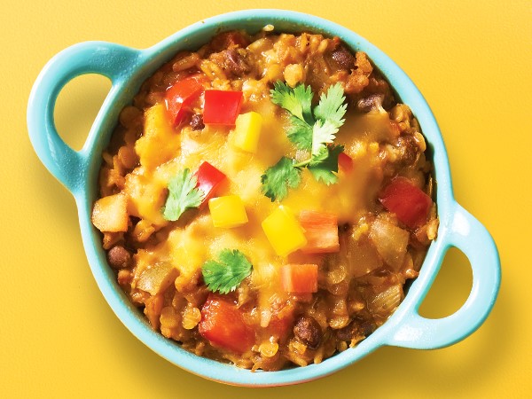 Lentil and brown rice topped with Cheddar cheese and dice bell peppers in a blue round dish with handles on a yellow background.