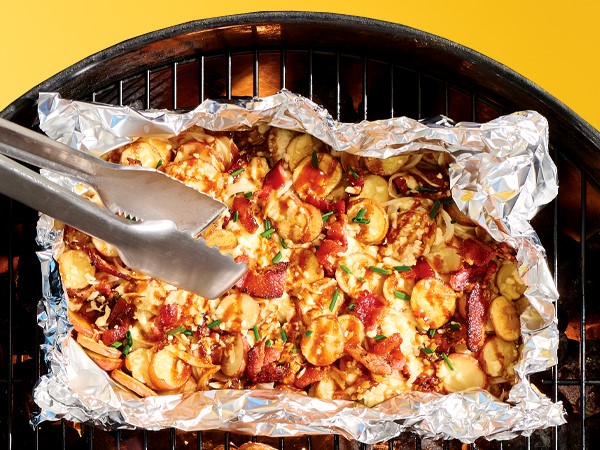 Cheesy barbecue grilled potatoes in a sheet of foil over a grill on a yellow background. 