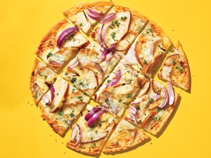 Gluten-free pizza with blue cheese, pear, and onions on a yellow background