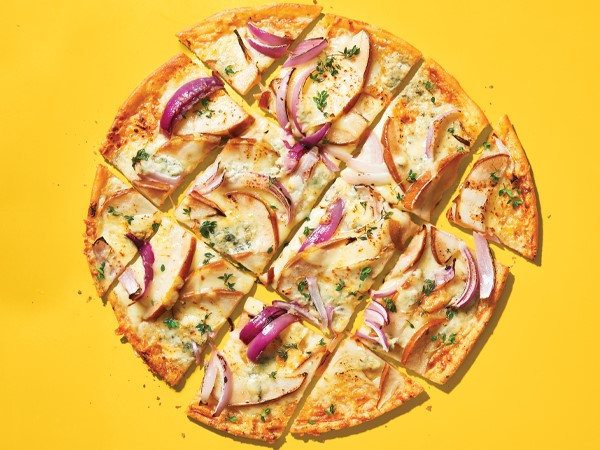 Gluten-free pizza with blue cheese, pear, and onions on a yellow background