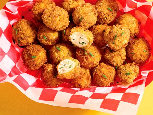 A basket full of fried goat-cheese balls on a white-and-red-checkered paper on a yellow background. 
