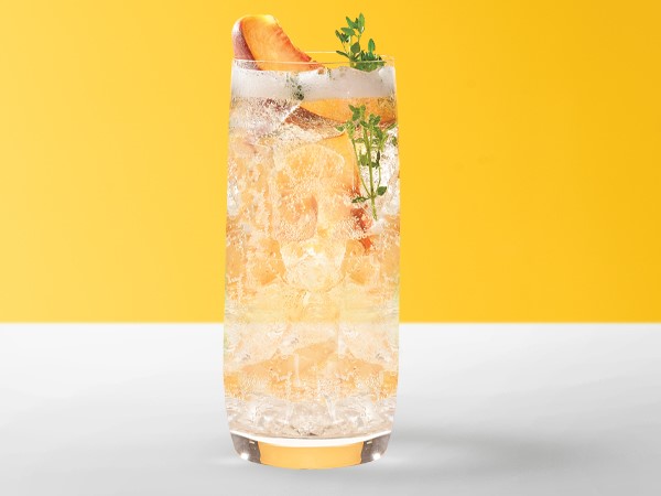 Ginger-peach spritzer in an ice-filled cocktail glass on a white and yellow background. 