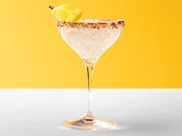 Spritzer margarita in a martini glass garnished with pineapple chunks on a white and yellow background.
