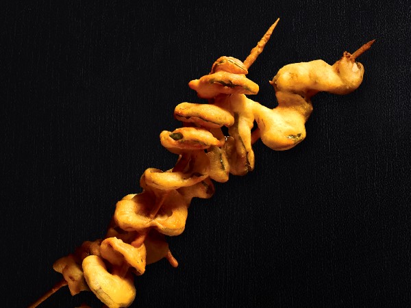 Two spiral fried pickles on sticks on a black background. 