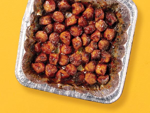 Brat burnt ends in a tin-foil square container on a yellow background.