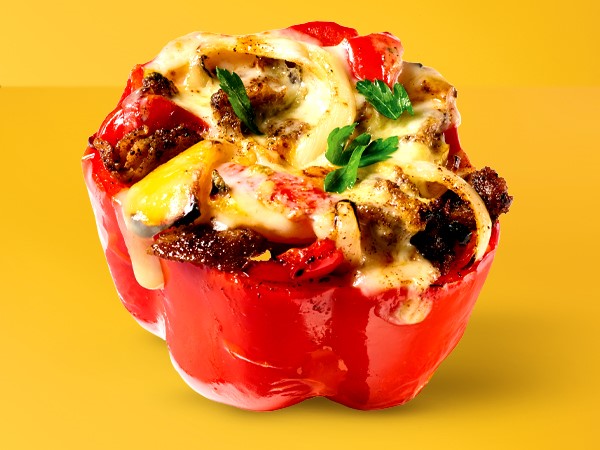 Cheesesteak filling in a red bell pepper on a yellow background. 