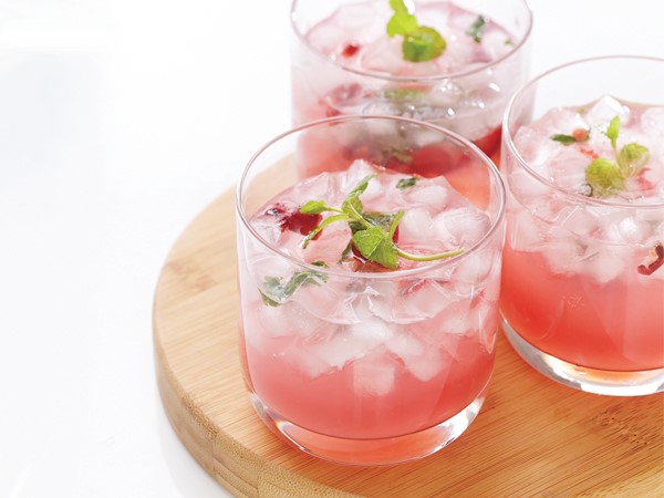 Three glasses of cherry mojitos centered on a wooden serving plate on a white background.