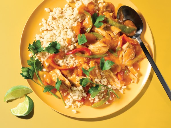 Coconut chicken curry on a yellow plate with a spoon and lime wedges on a yellow background.