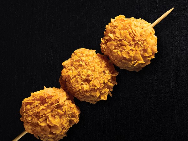 3 fried cheese balls on a stick on a black background.