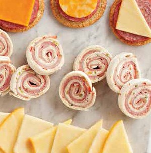 Cream cheese and ham pinwheels next to sliced cheese, meat and crackers