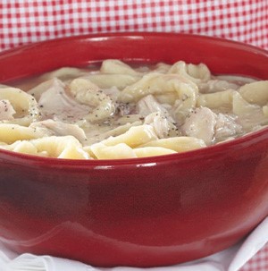 Red bowl filled with chicken noodle soup and garnished with fresh black pepper