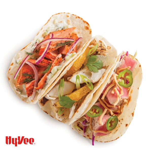 Three flour tortilla tacos filled with various sea food, mixed vegetables, and fruits