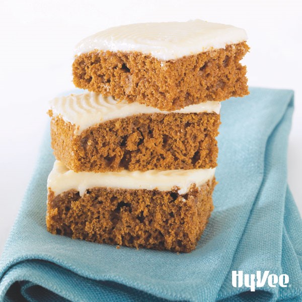 Cut and stacked pumpkin bars with cream cheese frosting on a blue napkin