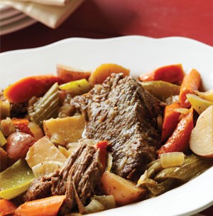 Bowl of pot roast surrounded by roasted vegetables