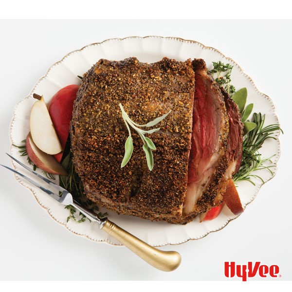 White plate with herb crusted prime rib garnished with fresh herbs and sliced red apples