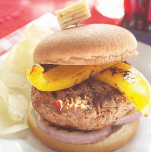 Burger served on plate, topped with pepper jack cheese cube on toothpick and side of potato chips