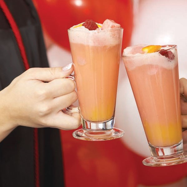 Glasses filled with orange and red raspberry orange punch with foam  at the top and topped with orange wedge and whole raspberry