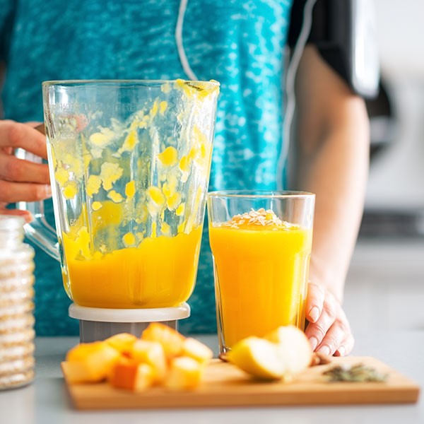 Person holding blender and cup of orange pumpkin smoothies