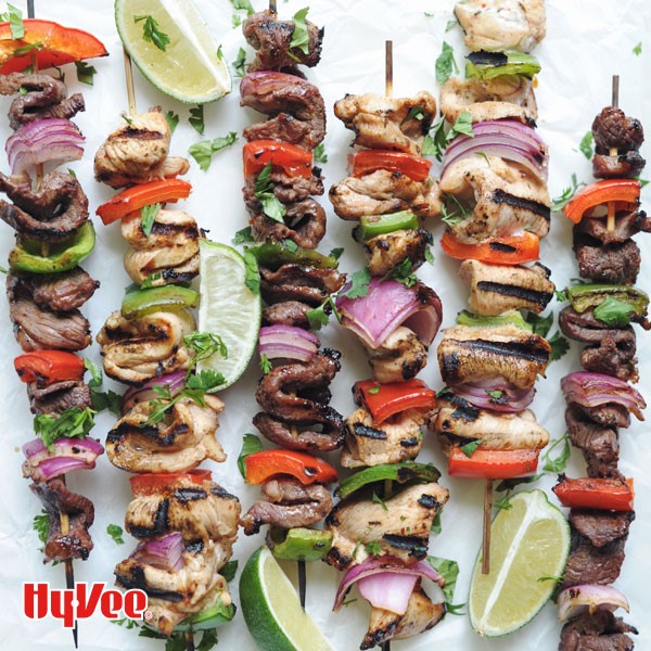 Chicken and beef fajitas on wooden skewers layered with green and red bell peppers and red onions with lime wedges on side