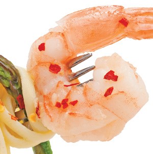 Cooked shrimp  with tail on a fork garnished with red pepper flakes