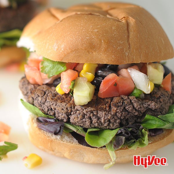 Bun topped with mixed greens, black bean burger patty, tomatoes, black beans, corn and onions