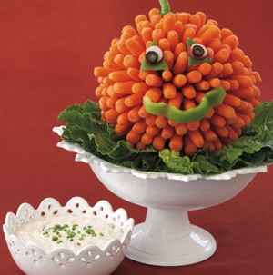 White cake stand topped with lettuce and carrots to look like a pumpkin and white dip on the side