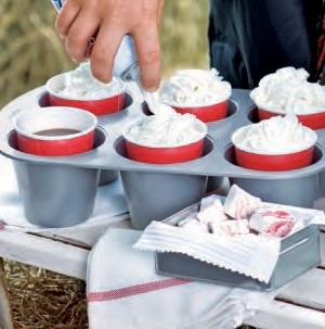 Popover pan filled with red solo cups holding hot cocoa and whipped cream topping
