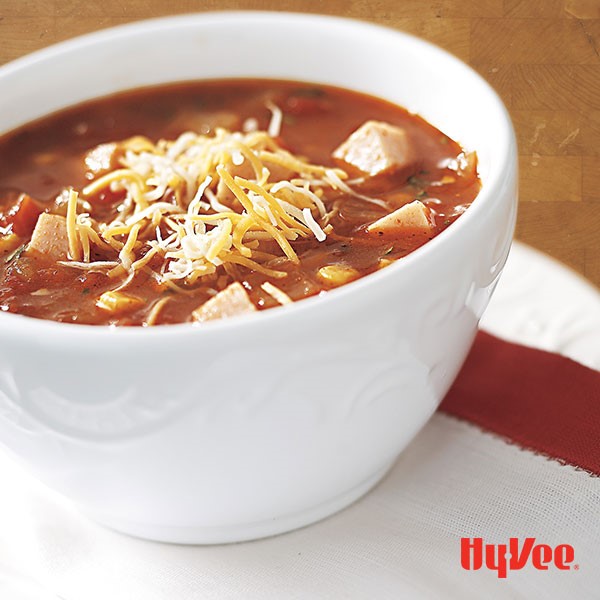 White bowl filled with tomato turkey tortilla soup and garnished with shredded cheese