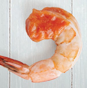 Tail on cooked shrimp dipped in cocktail sauce
