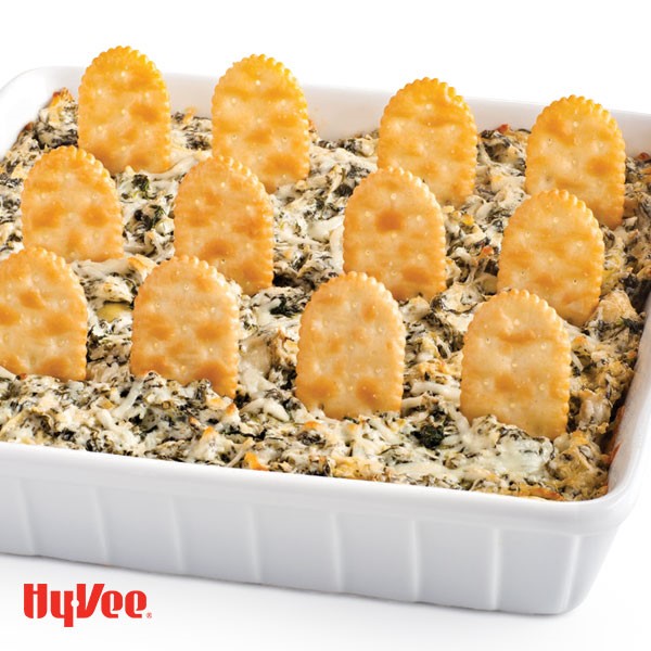 White casserole pan filled with spinach and artichoke dip with crackers sticking out