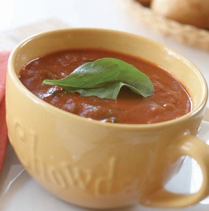 Yellow mug filled with tomato soup and fresh basil leaf as garnish