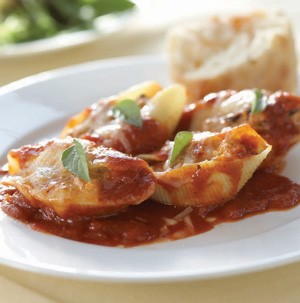 Stuffed shells on a white plate topped with red sauce and basil leaves