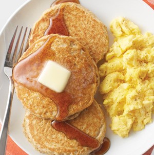Small round pancakes topped with butter square and maple syrup with scrambled eggs on the side