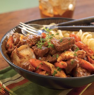 Beef, spiral pasta, and carrots in a bowl with a fork and a spoon